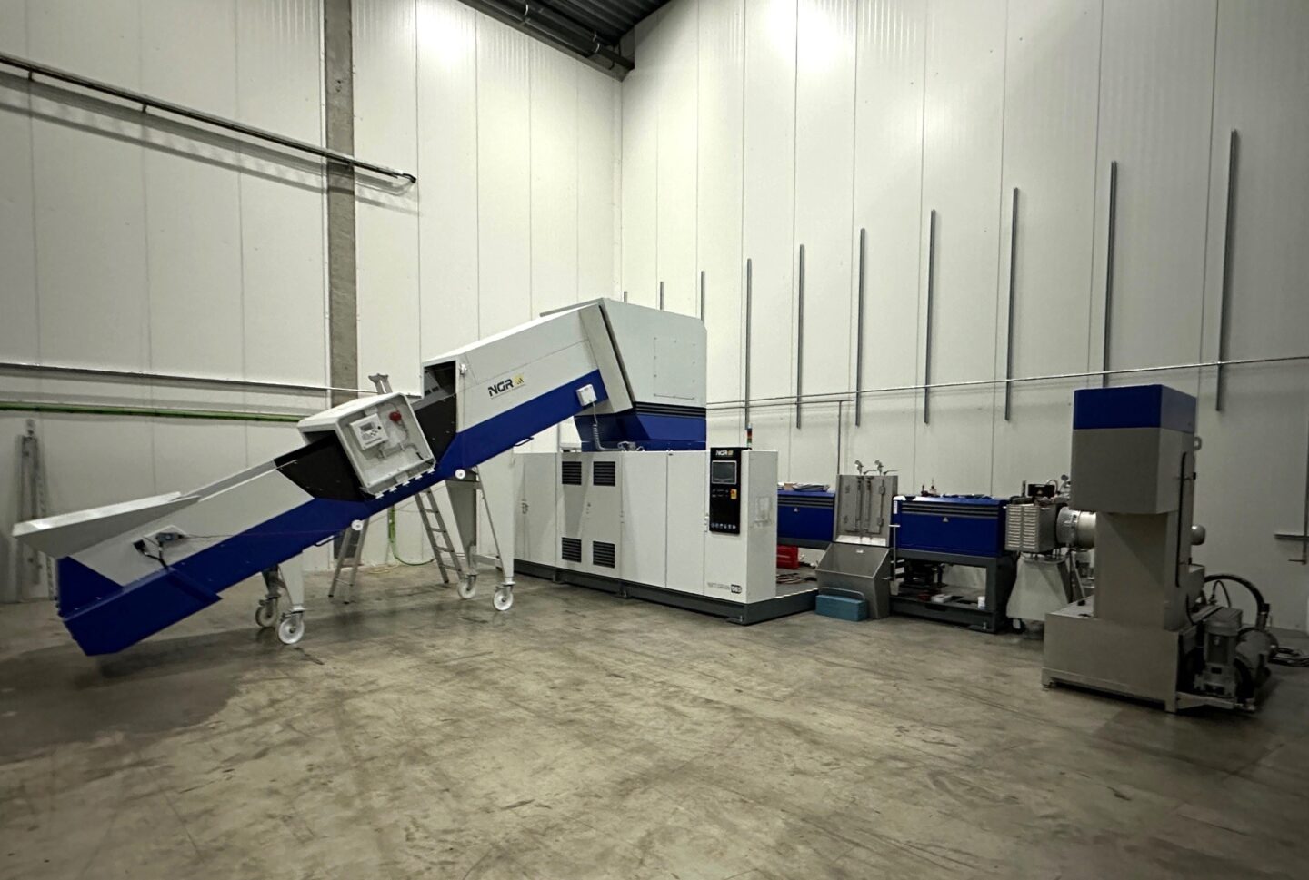 Seit mittlerweile vier Jahrzehnten zählt die AST Kunststoffverarbeitung GmbH zu den wichtigsten Akteuren in der Herstellung von geblasenen Kunststoffverpackungen, insbesondere von Kunststoffkanistern und -fässern mit Gefahrgutzulassung. Als familiengeführtes Unternehmen hat AST seit der Gründung im Jahr 1977 einen festen Platz in der Branche eingenommen und setzt dabei konsequent nicht nur auf Qualität, sondern auch auf eine nachhaltige Produktion. Mit Niederlassungen in Deutschland, UK, Belgien, Polen und den Niederlanden hat sich das Unternehmen auf das Management von Verpackungen spezialisiert – angefangen von der Lieferung bis hin zur fachgerechten Aufbereitung sämtlicher Industrieverpackungen. Ein wichtiger Bestandteil ihres Engagements ist auch ein Rücknahme- und Recyclingsystem namens Cipacks, das gebrauchte Gebinde zurücknimmt, reinigt und entweder als Rohstoff oder als vollständiges Produkt wieder verwendet. 
Langjähriges Vertrauen in bewährte Technologie 
Um die bei der Herstellung anfallenden Rückstände nahtlos in den Produktionskreislauf zurückzuführen, hat AST erneut auf die bewährte Schredder-Feeder-Extruder Kombination der Next Generation Recyclingmaschinen GmbH (NGR) gesetzt. Diese langjährige Partnerschaft wurde kürzlich durch die Investition in eine vierte NGR-Maschine, die NXT:GRAN 085-70 V HD, gestärkt. Mit einer Verarbeitungskapazität von bis zu 430 kg/h für LDPE-Folien und Klumpen sowie HDPE-Kanisterabfälle markiert dieser Meilenstein nicht nur den Erfolg der vergangenen Jahre, sondern festigt auch die gemeinsame Vision für eine nachhaltige Zukunft.
Um eine optimale Leistung und Effizienz zu gewährleisten, wurde NXT:GRAN 085-70 V HD genau an die Anforderungen von AST angepasst und mit verschiedenen Individualisierungen versehen.
Die Maschine mit Sonderlackierung wurde mit einem speziellen Förderband mit integriertem Metalldetektor ausgestattet, um Metallverunreinigungen während des Recyclingprozesses zu erkennen und zu entfernen. Durch ein Webcam-System am Beschickungstrichter kann der Materialfluss permanent überwacht und Abweichungen frühzeitig erkannt werden. Eine modulare Entgasungseinrichtung sorgt für die effektive Entfernung überschüssiger Gase während des Extrusionsprozesses.
Zusätzlich sorgt ein Siebwechsler und einen Vakuumpumpenstand für eine optimierte Leistung. Die Maschine wurde zudem mit einer Heißabschlaggranulierungseinheit ausgestattet, die eine schnelle und effiziente Granulierung des recycelten Materials ermöglicht und hochwertige Pellets garantiert. Eine Nachfolgeeinheit gewährleitet den reibungslosen Übergang zur nächsten Phase des Produktionsprozesses.
NXT:GRAN für hocheffizientes Post Industrial Recycling
Die von NGR patentierte Schredder-Feeder-Extruder-Kombination setzt auf die ONE-STEP-Technologie und vereint Zerkleinern, Zuführen und Extrudieren in einem Arbeitsgang. Mit über 1000 patentierten Shredder-Feeder-Extruder-Kombinationen weltweit hat sich die NXT:GRAN als Garant für höchste Leistung und Zuverlässigkeit etabliert. Die Schredder-Feeder-Extruder-Kombination ermöglicht eine Zero-Waste-Produktion und gewährleistet dabei den vollen Werterhalt des Materials, während gleichzeitig der Arbeits- und Energieaufwand auf ein Minimum reduziert wird.
Durch die Steigerung der Schneidleistung im Schredder kann die Maschine auch große, dicke oder sperrige Teile ohne vorherige Zerkleinerung verarbeiten, was ihre Vielseitigkeit und Flexibilität maßgeblich erhöht.  Eine optimierte Materialzufuhr zum Extruder, die formschlüssig zur Extruderschnecke angeordnet ist, sorgt bei der NXT:GRAN für zusätzliche Power. 
Die EIN/AUS-Einknopfautomatik ermöglicht ein einfaches Anfahren und Abstellen der Maschine sowie ein sanftes Anlaufen der Komponenten. Selbst nach unvorhergesehenen Abschaltungen kann die Maschine in weniger als zwei Minuten wieder in Betrieb genommen werden.
Dank des Dump-and-Run-Betriebs wird der Materialfüllstand im Trichter permanent gemessen und die Zufuhr entsprechend gesteuert, was einen kontinuierlichen Betrieb ermöglicht und die Produktivität weiter steigert.